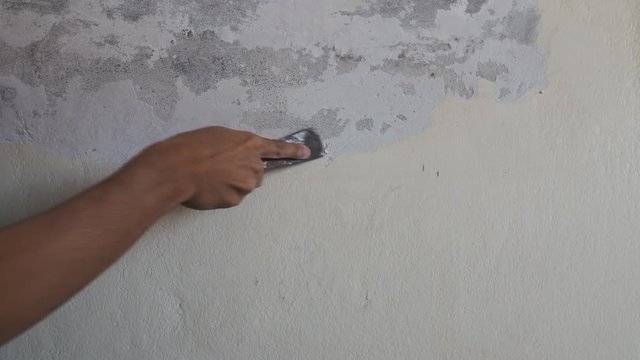 Removing old paint from the wall with a metal spatula, Hand of worker scraping old paint on concrete wall. Remover old paint. Manual work with scraper. preparation for painting a room