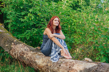 Romantic happy woman sitting on the dry fallen tree with bare feet