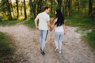 Fototapeta premium Loving guy and girl run through the forest, in nature, in tracksuits for a walk, holding hands. Love story newlyweds. Photography, concept.