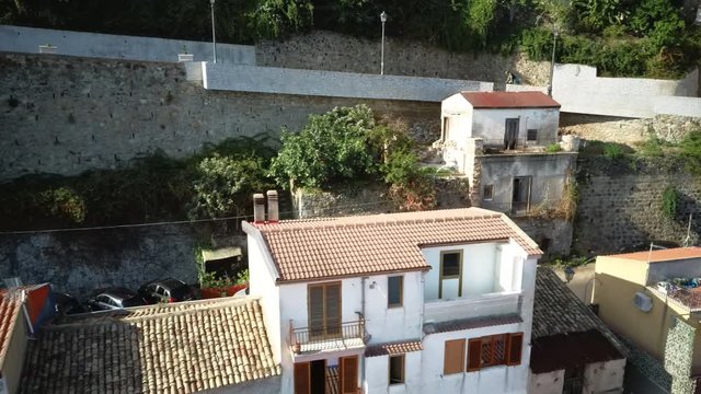 Aerial view of unrecognized cyclist climbing to the top of a hill, around medieval European stone houses. Day flight over medieval European houses of southern Italy