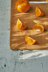 Pieces of mandarin on wooden board in morning sun rays, on white table