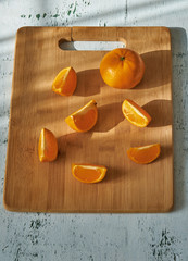 Pieces of mandarin on wooden board in morning sun rays, on white table