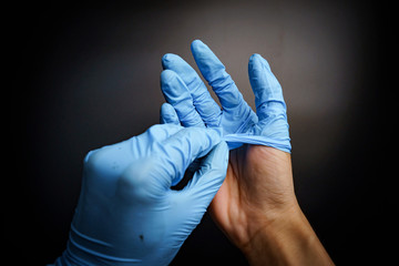 Human hands in blue surgical gloves by gesture take off hands isolated black background with a closeup shot