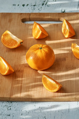 Pieces of mandarin on wooden board in morning sun rays, on white table