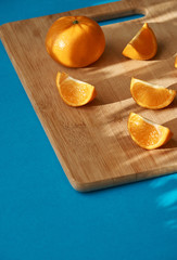 Pieces of mandarin on a wooden board in the morning rays of the sun, on a blue background