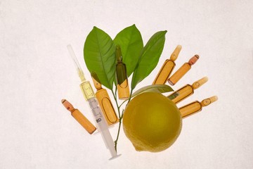 Vitamin C. Serum with Vitamin C  in ampoules and syringe, fresh  lemon with green leaves  on a...