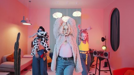 Zoom out shot of fancy female dancers in glamorous outfits performing vogue for camera in vintage studio with pink lighting