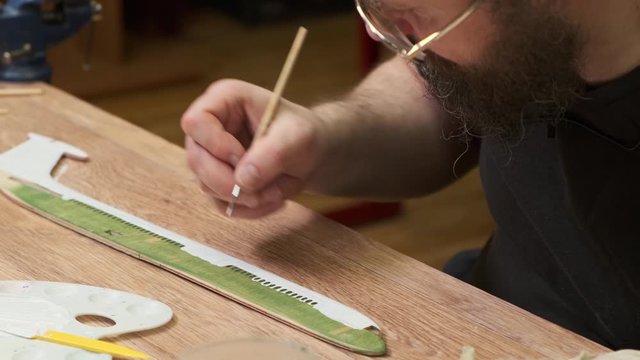 bearded master in glasses colours wooden fuselage between windows of vintage passenger jetliner model slow motion closeup