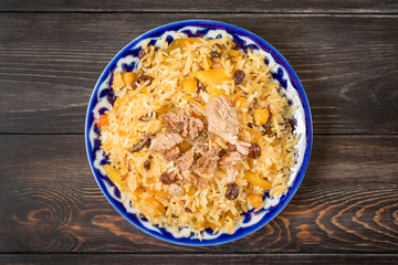 National food - uzbek pilaf with meat in plate with traditional pattern on dark wooden table Top view Flat lay Ramadan, Nowruz holiday concept