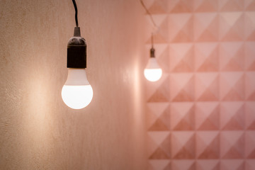 A glowing light bulb hangs on a wire in the house, blurred background.