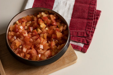 Tomate picado en tabla de madera con cuchillo grande rojo para preparación de comida con trapo en rayas rojo y blanco