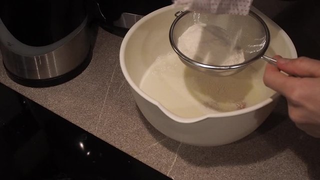 Adding flour to white bowl with milk through stainer