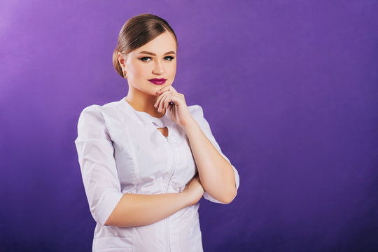 Beautiful girl in a medical coat. On a purple background. Studio photo nurse in white clothes