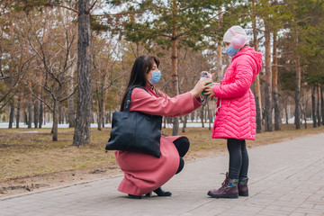 Mom and daughter walk in the park during quarantine of the coronavirus. Baby and parent in protective medical masks. A woman gives a child a toy. Pandemic COVID-19