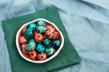 Painted red and blue quail eggs for Easter in small ceramic plate on gray linen textile background. Empty place for text and sign.