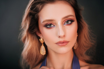 Portrait of a beautiful girl in a blue dress on a dark background. A model with professional makeup and clean skin. Fashion photography in the studio