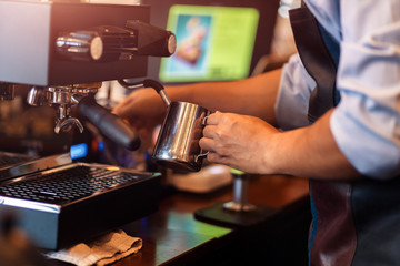 Barista steaming milk in the pitcher with coffee machine for  preparing to make latte art.