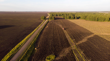 Aerial photography, red industrial machinery with a plow plowing  agricultural fields near a rural...