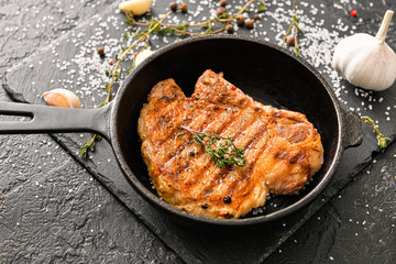 Frying pan with cooked pork steaks on dark background