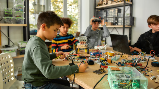 Imagine, create, participate. Young technicians building robots and vehicles, using soldering iron to join chips and wires, programming toys at a stem robotics class