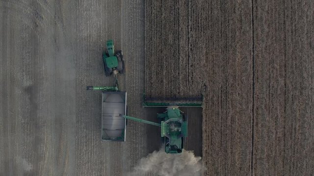 Top down drone view of combine harvester dumping grain into tractor and grain cart unit.