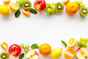 Fresh fruits background with citruses, apple, kiwi and grape on white table top-down frame copy space