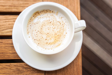 Cup of cappuccino coffee with soft microfoam on wooden table.