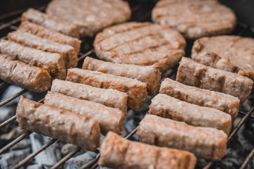 Balkan specialty - cevapcici, but made with chicken meat insted of beef or pork, which makes them recognizably lighter or whiter in color, lying on a metal grill above hot coal