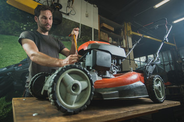 Professional serviceman is repairing a lawnmower, unscrewing a spark plug. Man repairing a mower in a workshop