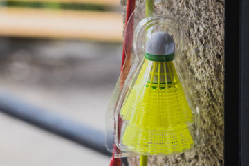 A yellow badminton ball resting on a wall next to a racket.