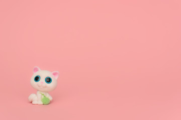 One cute white kitten with a ball of thread on a pink background. Kids toy cat with big blue eyes and a ball of thread in its paws on pink. Place for text. Minimalism. Sewing, needlework for children.