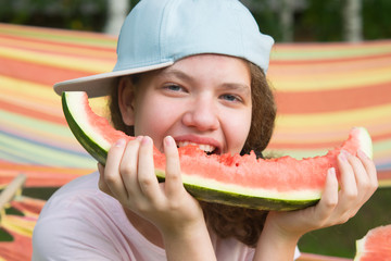 close-up, a cheerful little girl in a cap, eating a piece of watermelon, outdoors