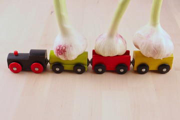 A toy, wooden, multi-colored train carries a crop of young garlic on a light wooden background....