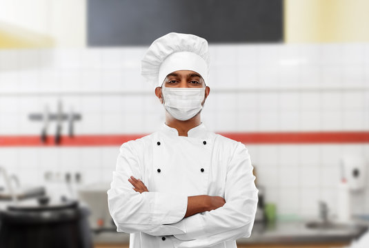 health, safety and pandemic concept - indian male chef cook in toque with crossed hands wearing face protective medical mask for protection from virus disease at restaurant kitchen