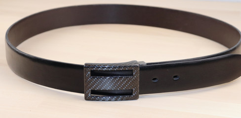 a stylish, leather belt in black and carbon fittings lies on a light background. Expensive gift...