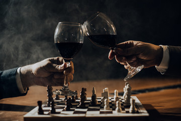 Close up of hands of men playing chess and drinking wine.