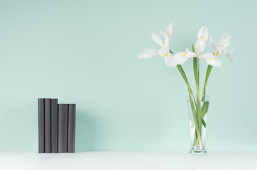 Spring soft students workplace with row black  books, fresh white flowers in trasparent glass vase on light white wood table and green mint menthe wall, copy space.