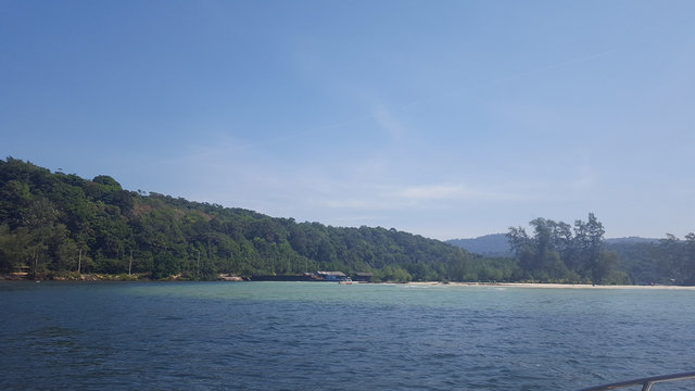 The photo was taken from a motor boat. View of the island, palm trees, ocean, spray, beach