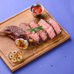 Sliced grilled Medium rare barbecue Steak on bone with spices served on a rustic wooden board over blue background.