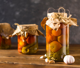 Homemade jars of pickled tomatoes and cucumbers on a rustic wooden background. Pickled and canned...