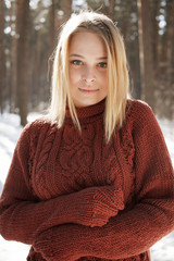 Portrait of a young beautiful blonde woman in sweater posing in winter park. Sunny day in forrest.