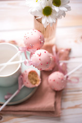 Obraz na płótnie Canvas Cake pops in a light key in a beautiful utensil with pink chocolate cream and flowers on a wooden background.