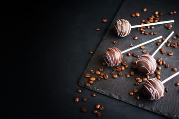 Delicious dessert with chocolate and milk cream on a stick with an atal tape. Cake pops on a slate board on a black background