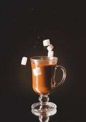 Coffee in glass cup with falling sugar on dark background