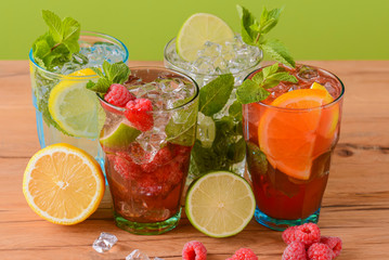 Four tropical mixed drinks, orange, lemon and raspberries cocktails over bright pastel green background.