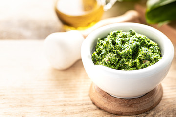 Wild leek pesto with olive oil and parmesan cheese in a white ceramic mortar on a wooden table. Useful properties of ramson. Copy space.