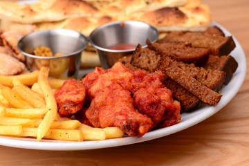 Big plate of beer snacks. Crispy fried chicken, french fries and different kinds of bread on white plate.