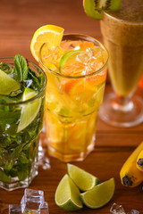 Three tropical mixed drinks, mint, lemon and kiwi fruit cocktails served on light wooden table.