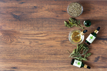 Green bottles of medical CBD oil with cannabis seeds and dried leaves top view on wooden background. Alternative medicine concept.