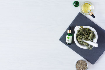 Green bottles of medical CBD oil with cannabis seeds and dried buds top view on white background. Alternative medicine concept.